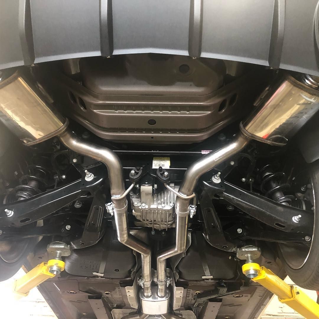 Underbody view of a car on a lift, showing exhaust, suspension, and yellow lift arms