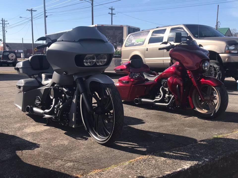 Two custom motorcycles parked in a sunny lot, one matte black and one red.