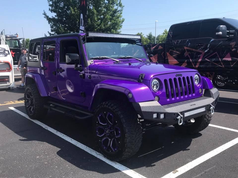 Purple lifted Jeep Wrangler parked in a lot, with black rims and dark off-road tires.