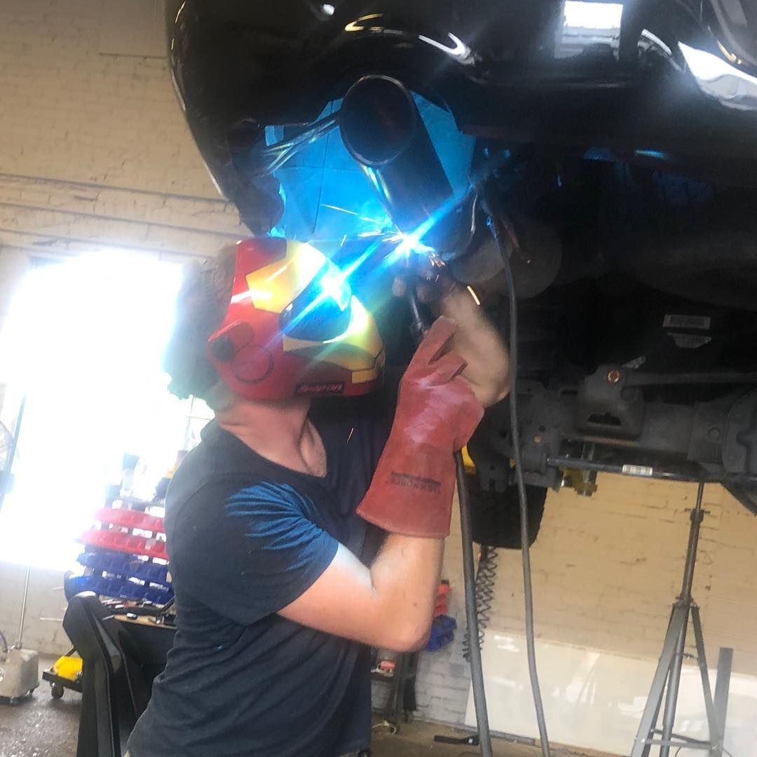 Person wearing a welding helmet and gloves works under a vehicle in a garage.