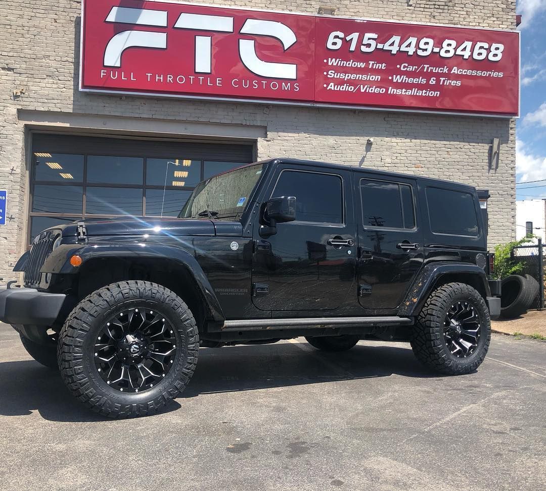 Black Jeep Wrangler parked outside a shop with a red FTS sign.