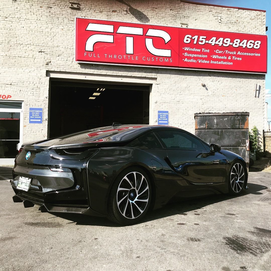 Black sports coupe parked outside an FTC auto shop with a red sign above the garage.