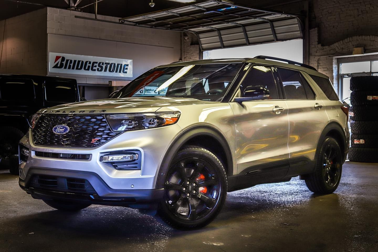 Silver SUV parked indoors under showroom lights, with a Bridgestone sign in the background