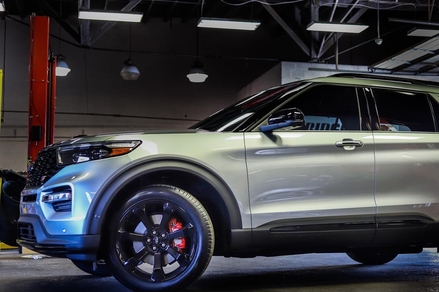 Silver SUV parked indoors under showroom lights, side view with black rims and red brake calipers