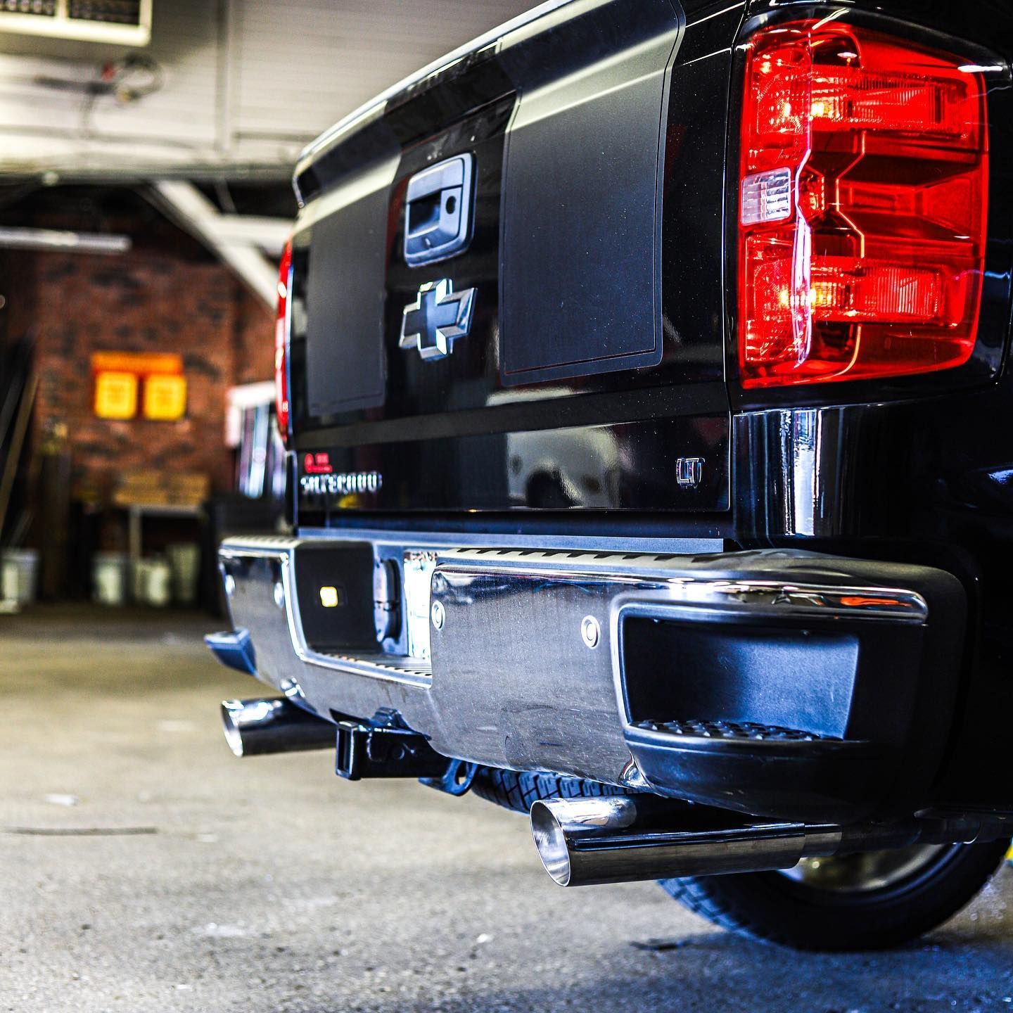 Rear view of a black Chevrolet pickup truck parked in a garage, with chrome bumper and red taillights.