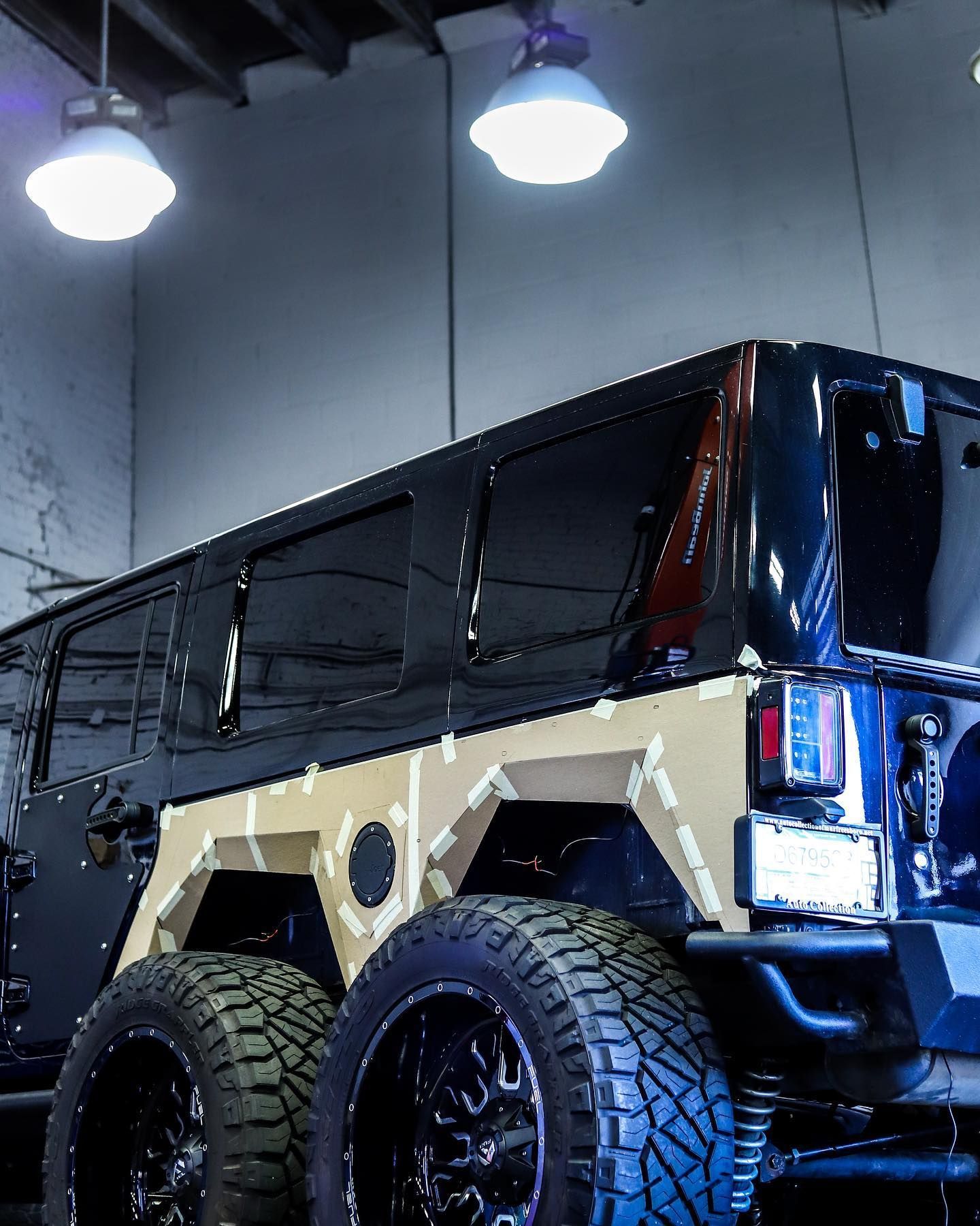 Black customized off-road SUV with oversized tires inside a garage, viewed from the rear side