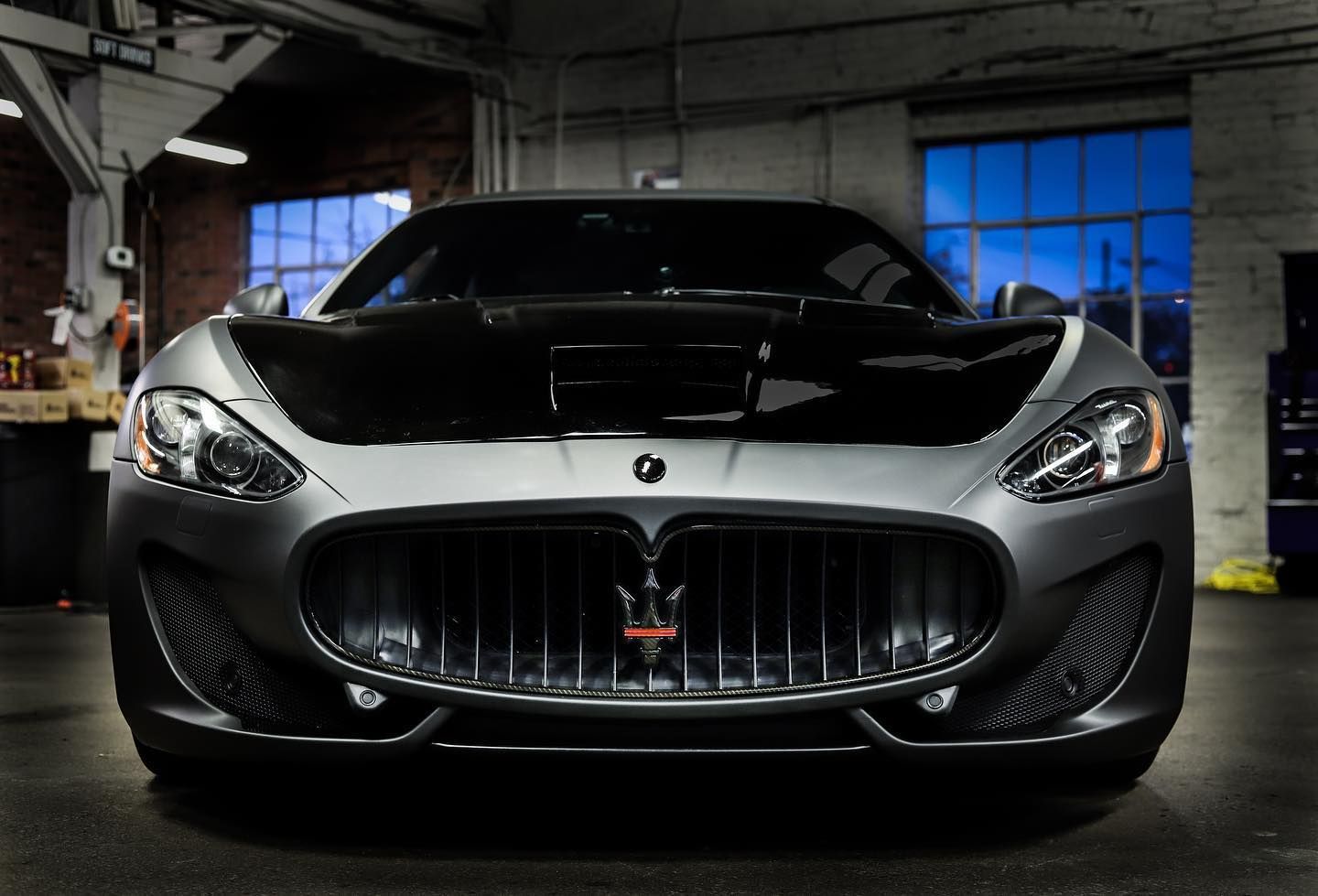 Front view of a black sports car in a dim garage with blue-lit windows