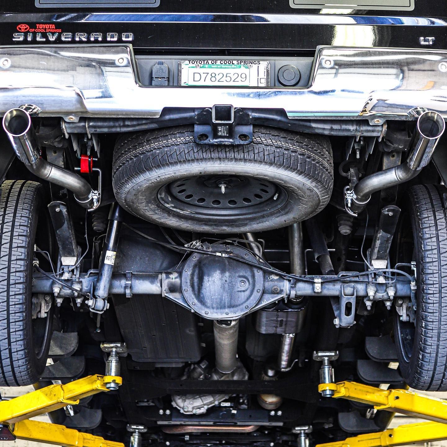 Rear underside of a car on a lift, showing exhaust, spare tire, and suspension components.