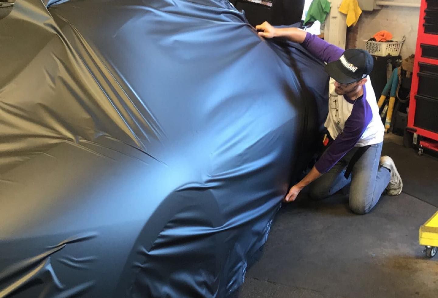 Two people kneel and tug at a large black inflatable object in a workshop.