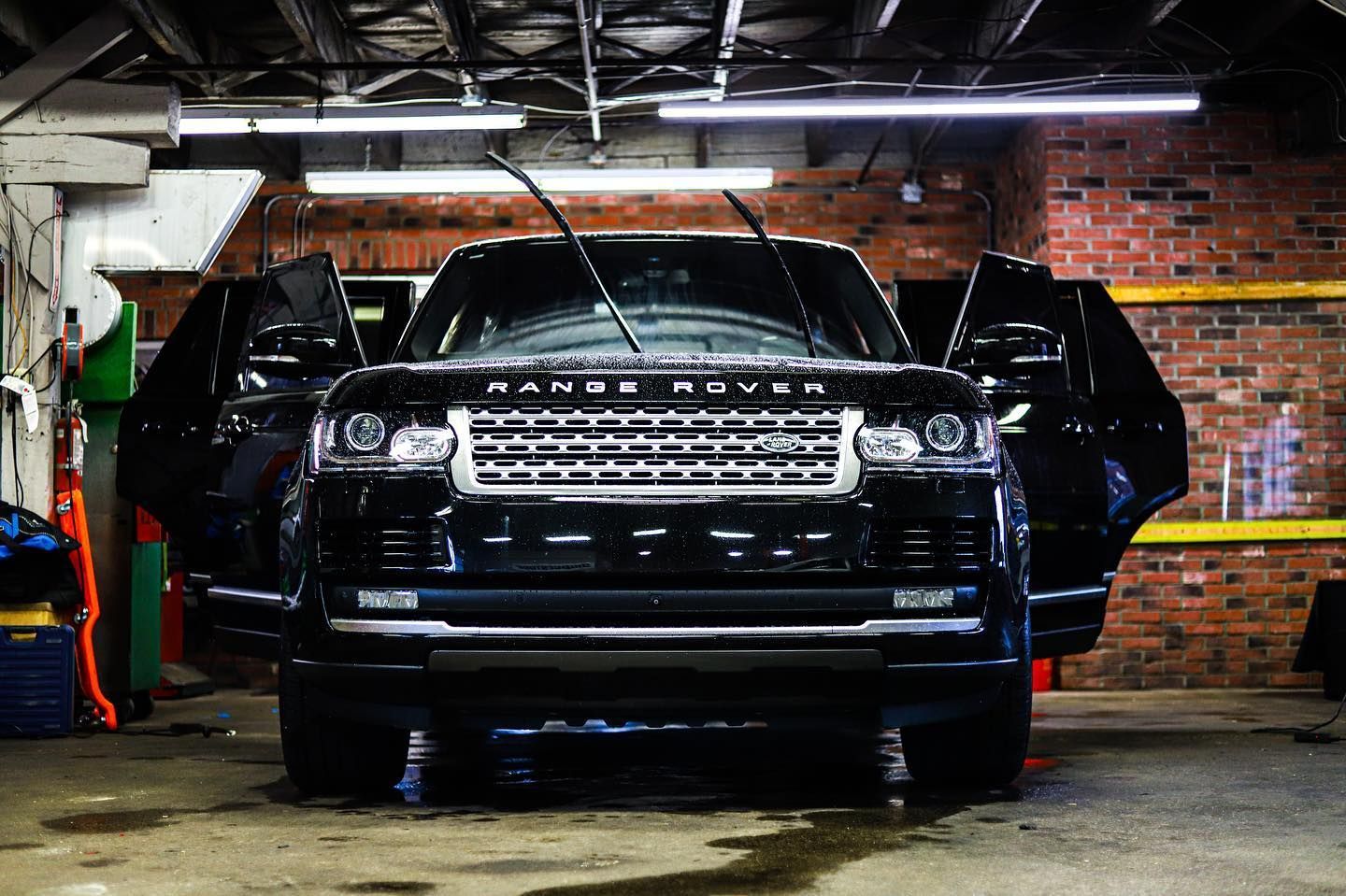 Black SUV in a garage, front doors open, with a brick wall and overhead lights in the background.