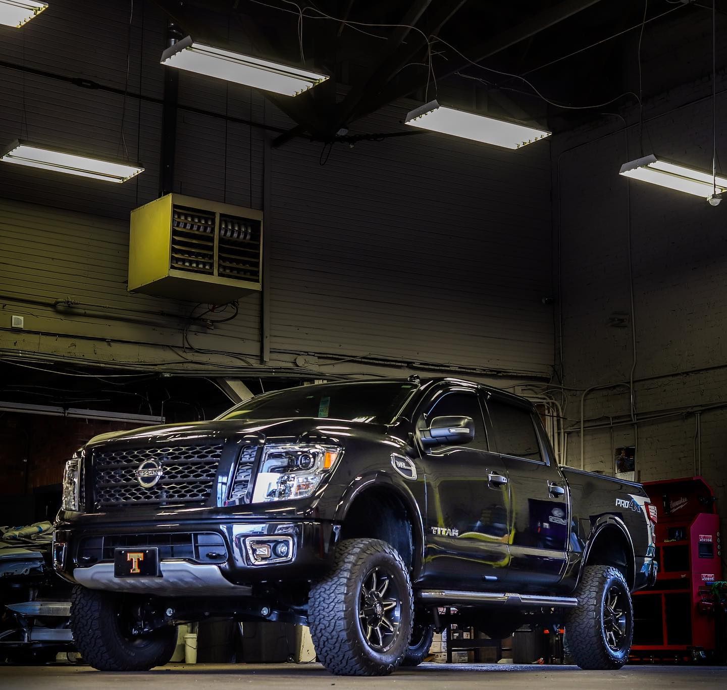 Black lifted pickup truck in an auto shop garage under bright overhead lights.
