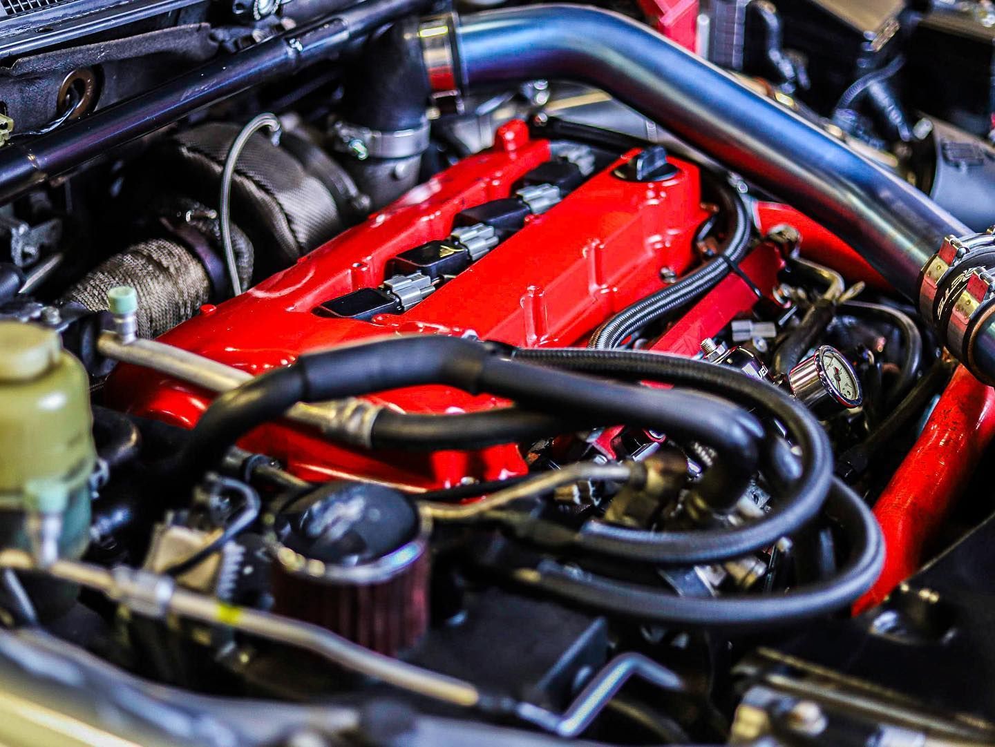 Close-up of a car engine bay with red valve covers and black hoses