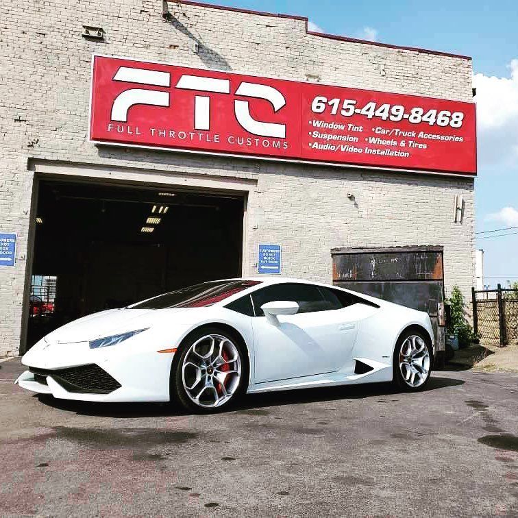 White sports car parked outside an FTS auto shop with a red sign and open garage door