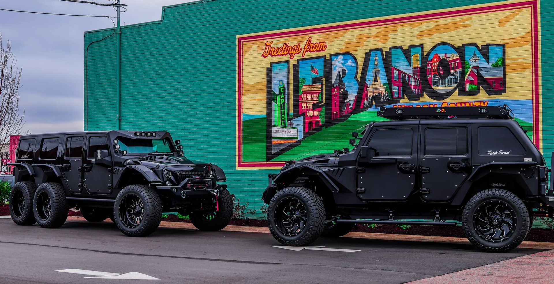 Two black off-road vehicles parked beside a colorful “HERANCIO” mural on a city street
