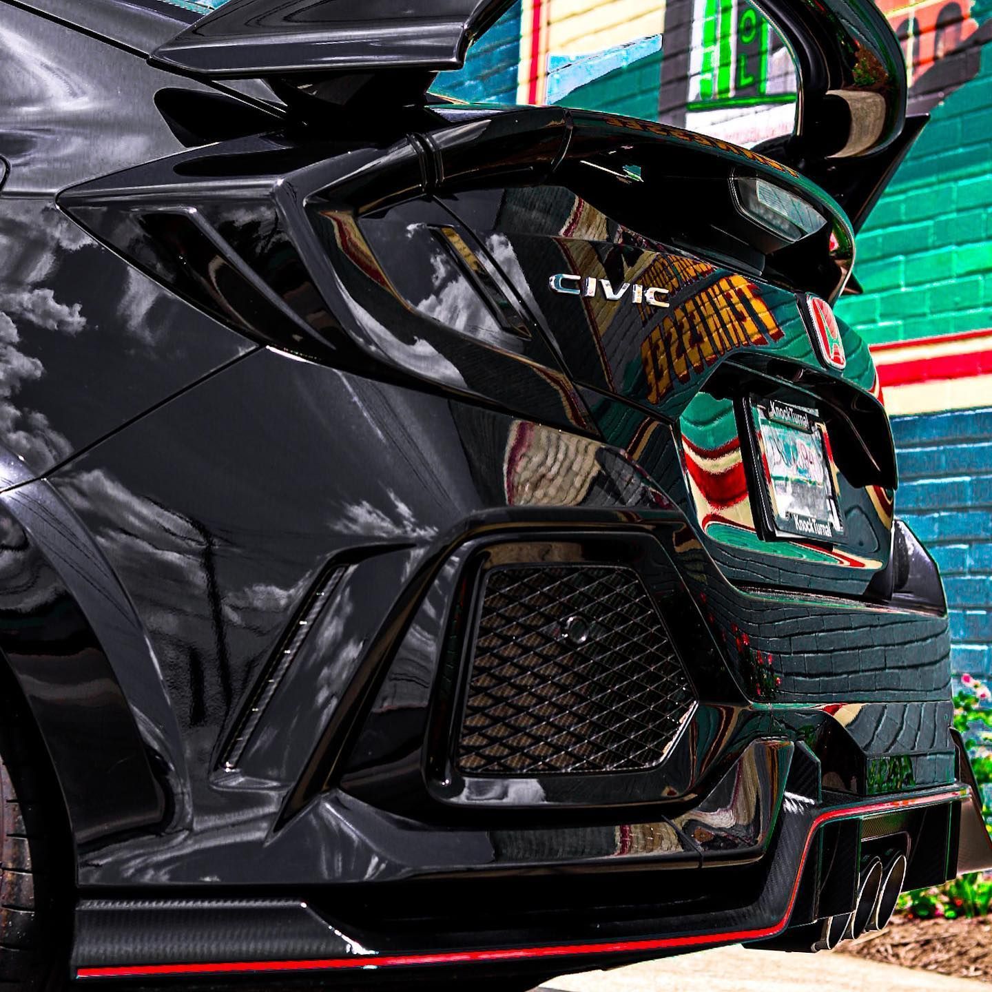 Rear view of a black Honda Civic with red accents, parked beside a colorful brick wall