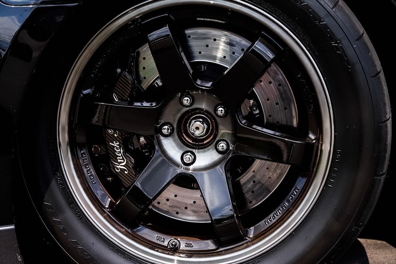 Close-up of a black car wheel rim with wet spokes and brake rotor visible behind it