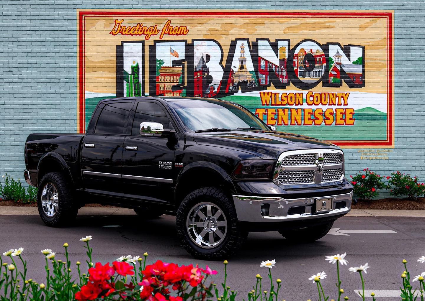 Black pickup truck parked before a Lebanon, Wilson County, Tennessee mural with flowers in front