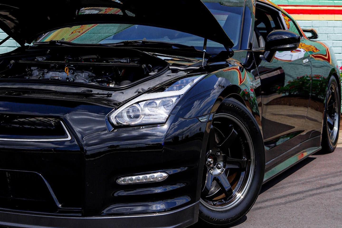 Dark blue sports car parked outdoors with its hood open and a black wheel visible