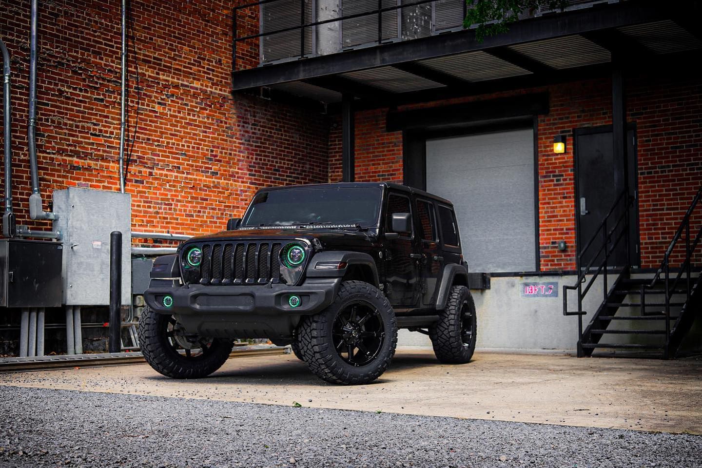 Black Jeep Wrangler parked beside an industrial brick building with a loading dock.