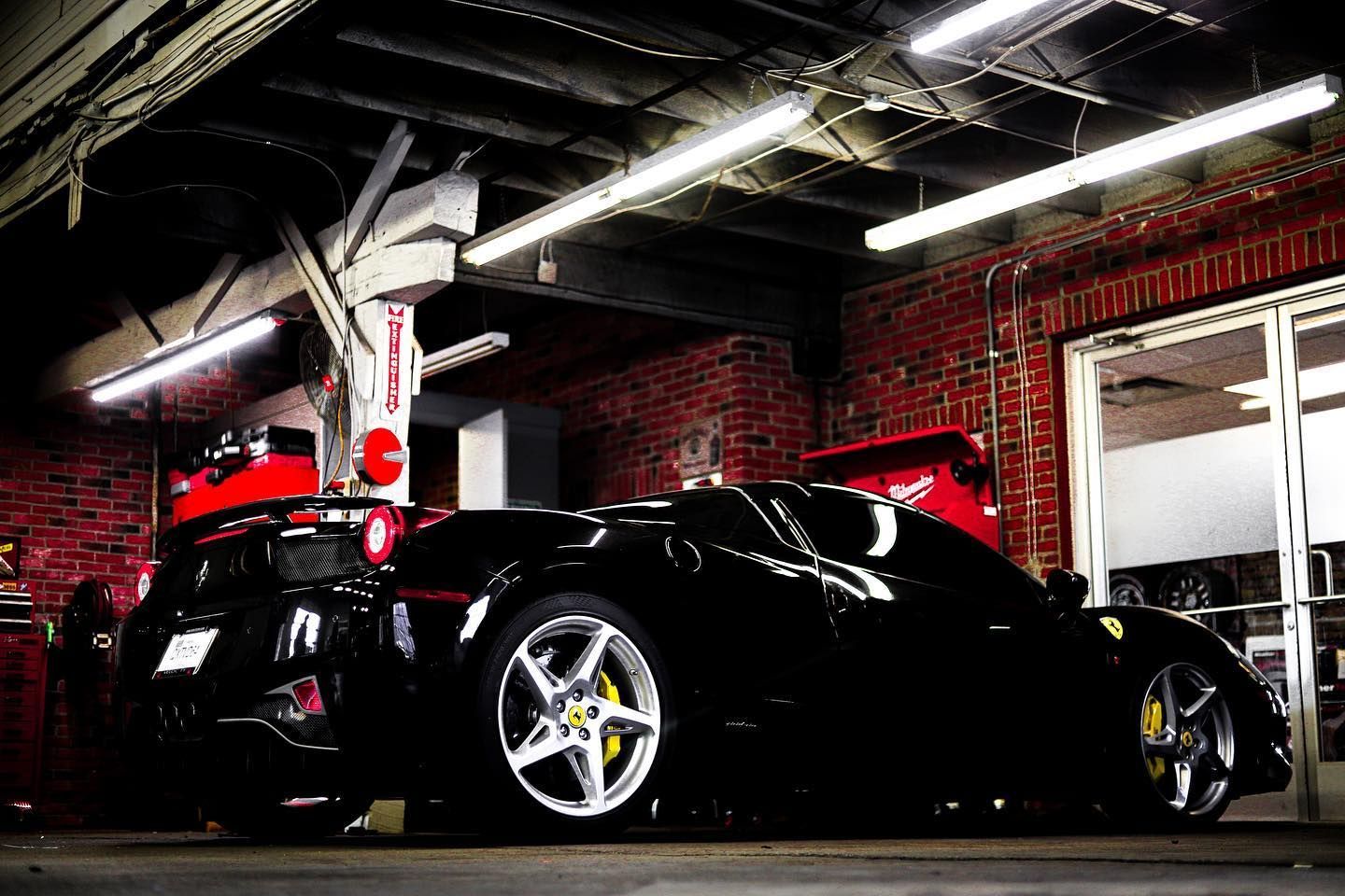 Two sleek sports cars parked in a dim brick garage with bright overhead lights