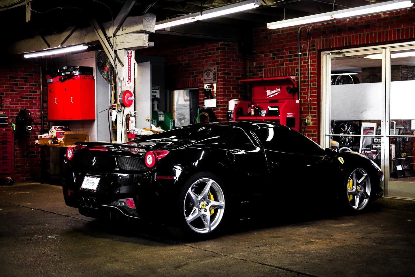 Black sports car in a dim garage with red walls and bright overhead lights