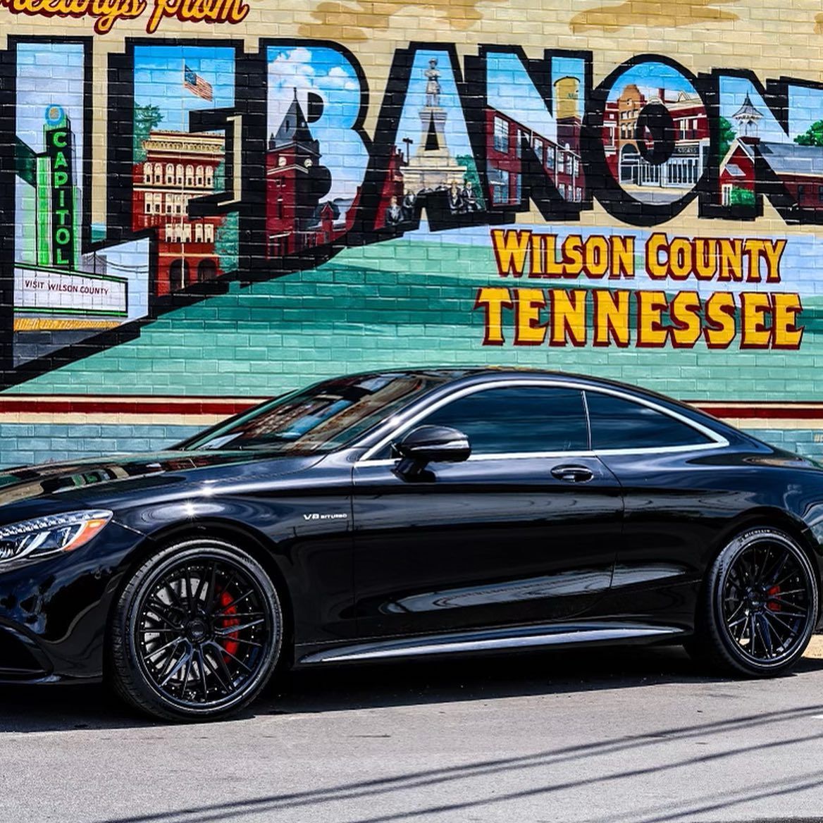 Black sports coupe parked before a Lebanon, Tennessee mural with colorful lettering.