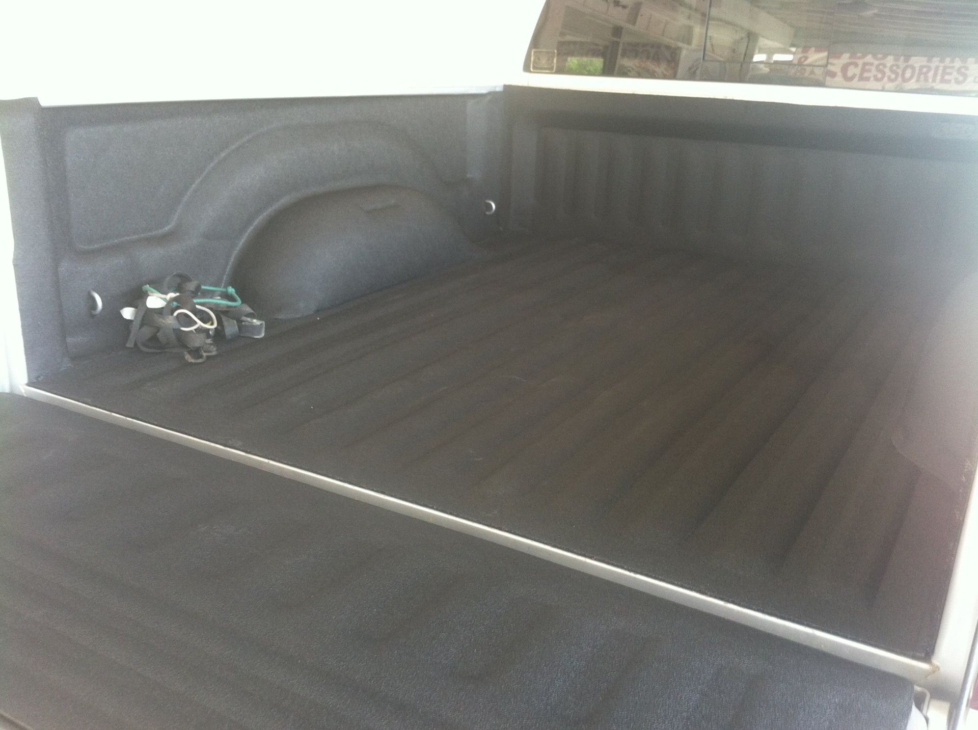 Empty pickup truck bed with a black liner and a small bag in the corner.