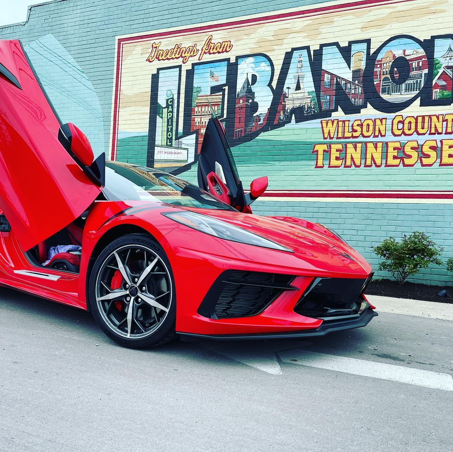 Red sports car with scissor doors open parked in front of a Lebanon, Tennessee mural.