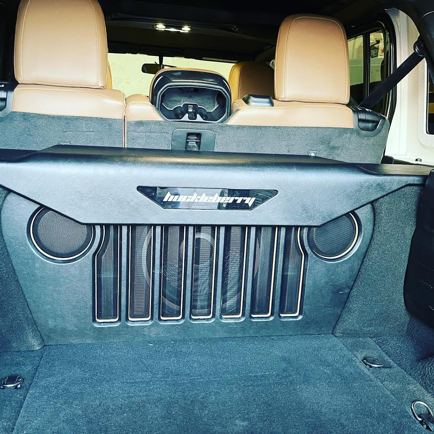 Trunk-mounted speaker box in a tan-lined SUV cargo area with a central goggles-like display panel.