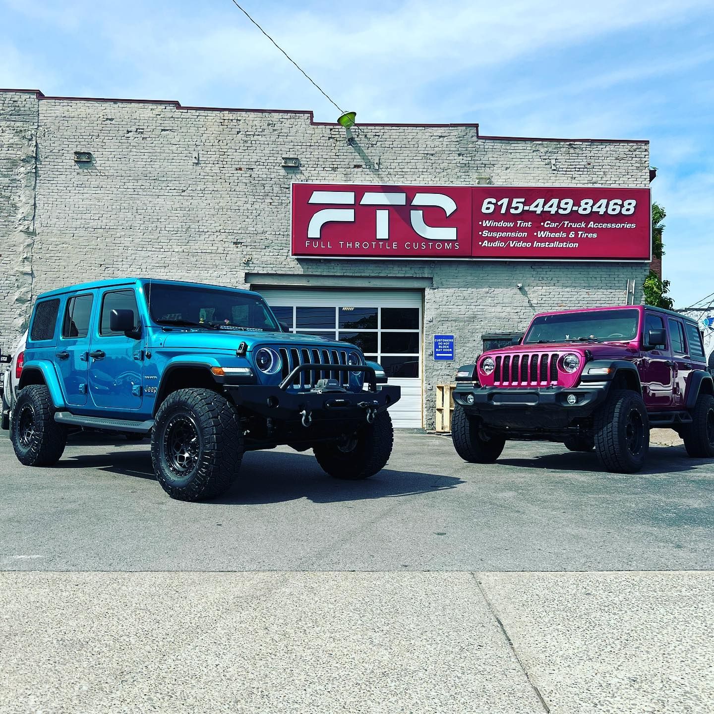 Blue and magenta lifted Jeep Wranglers parked outside an FTO auto shop sign