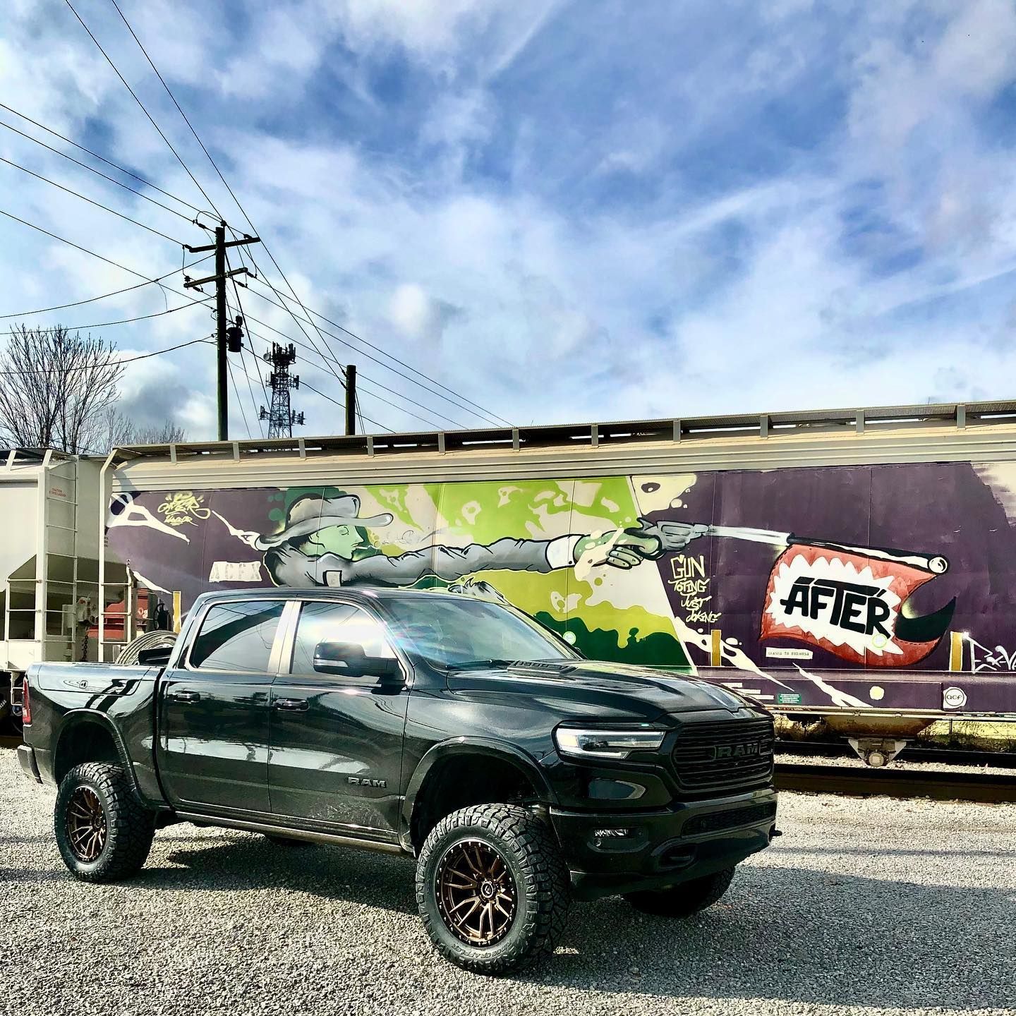 Black pickup truck parked in front of a colorful graffiti-covered train car under a cloudy sky