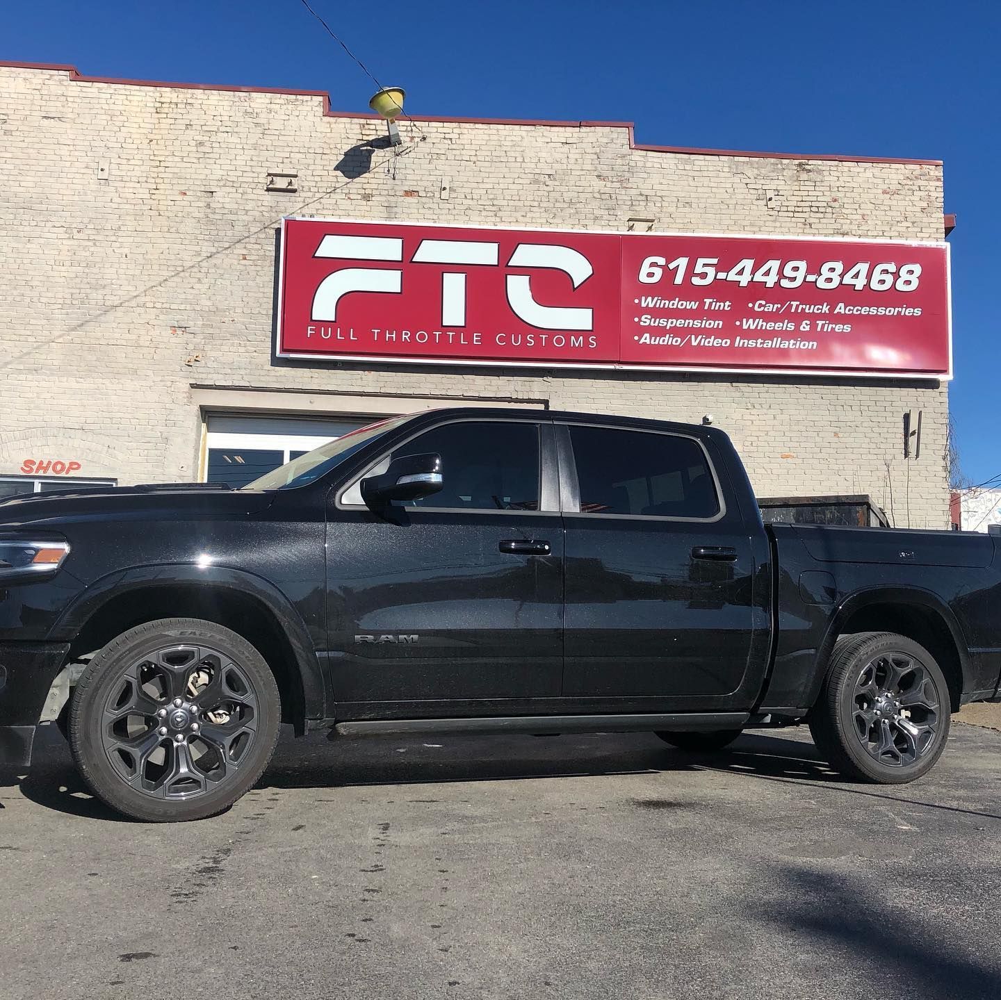 Black pickup truck parked in front of a brick building with a red FTS sign and phone number