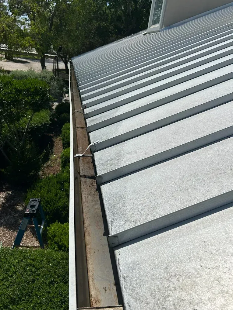 Close-up of a corrugated metal roof edge with trees and a driveway below