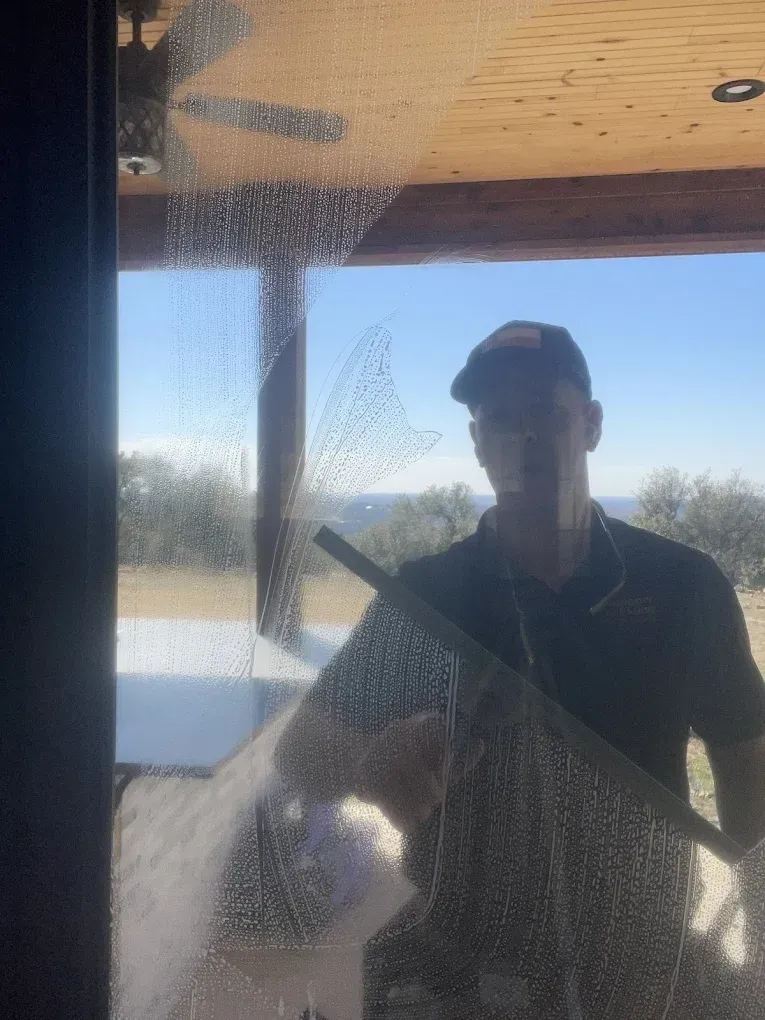 Person cleaning a window with a squeegee, silhouetted against a bright outdoor view.