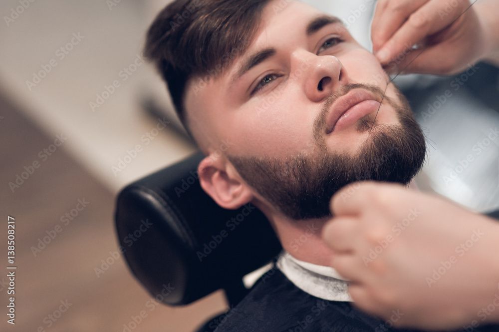 Un homme se fait épiler les sourcils par un coiffeur.