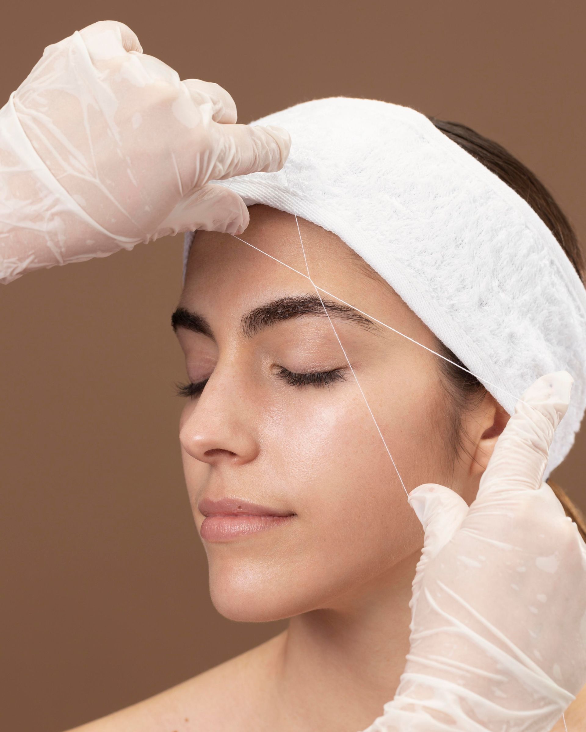 Une femme se fait dessiner les sourcils par une personne portant des gants.