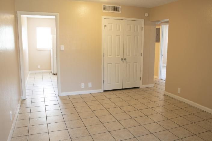 Empty beige-tiled room with white double closet doors and two open doorways to a bright hallway