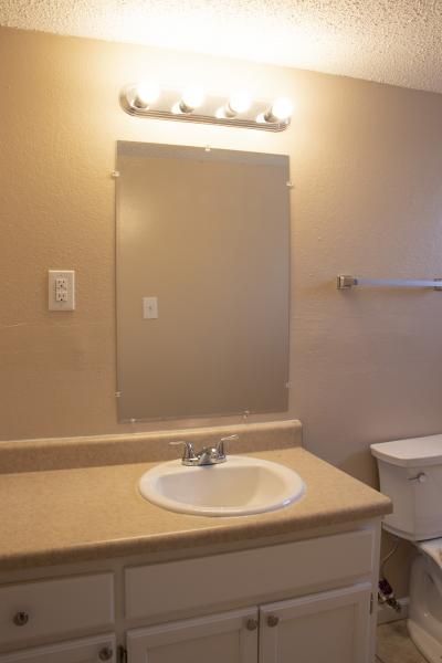 Bathroom vanity with sink, mirror, and overhead lights on beige walls