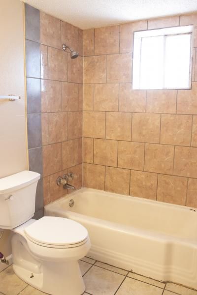 Bathroom with toilet, bathtub, beige tile walls, and a small window.