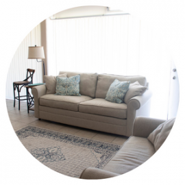 Bright living room with beige sofa, patterned rug, floor lamp, and sheer curtains by a window.