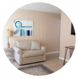 Cozy beige living room with armchair, lamp, abstract wall art, and tiled floor