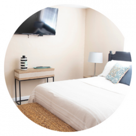 Bright bedroom with a white bed, bedside lamp, wood desk, and wall-mounted TV