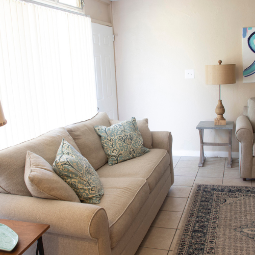 Beige sofa with patterned pillows in a bright living room beside a lamp and side table.