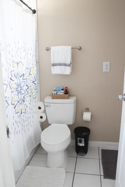 Small bathroom with toilet, shower curtain, towel rack, trash can, and tiled floor