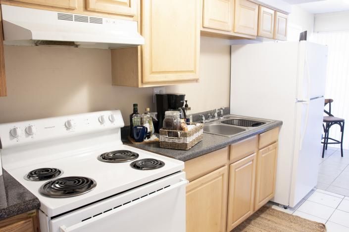 Small beige kitchen with white stove, light wood cabinets, and a refrigerator beside a counter and sink.