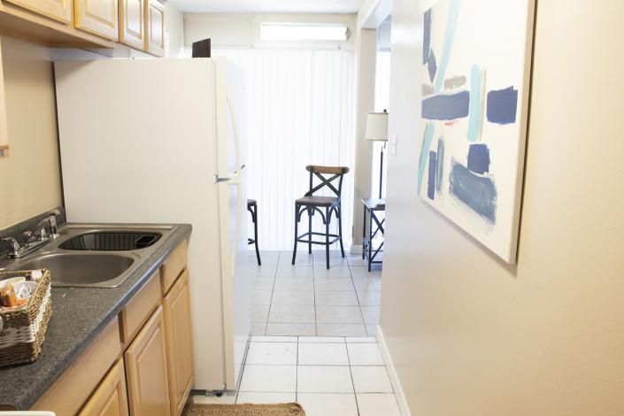 Narrow kitchen opening to a bright dining area with a table, chairs, and wall art