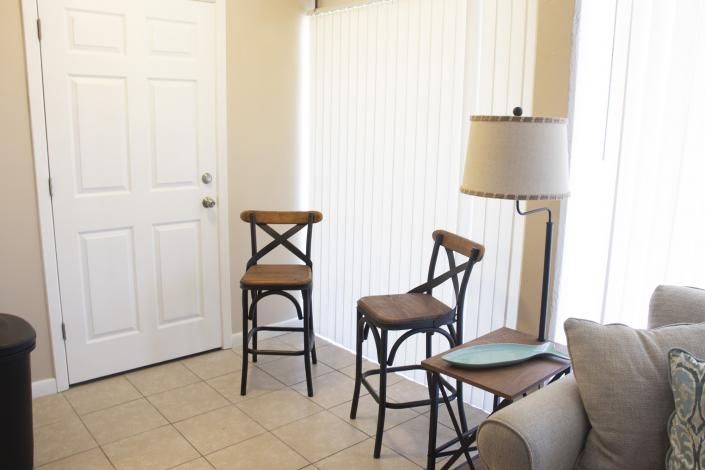 Small living room corner with two chairs, a floor lamp, a white door, and vertical blinds
