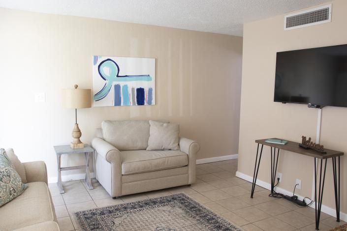 Bright living room with beige armchair, side table, wall art, patterned rug, and a TV on a stand