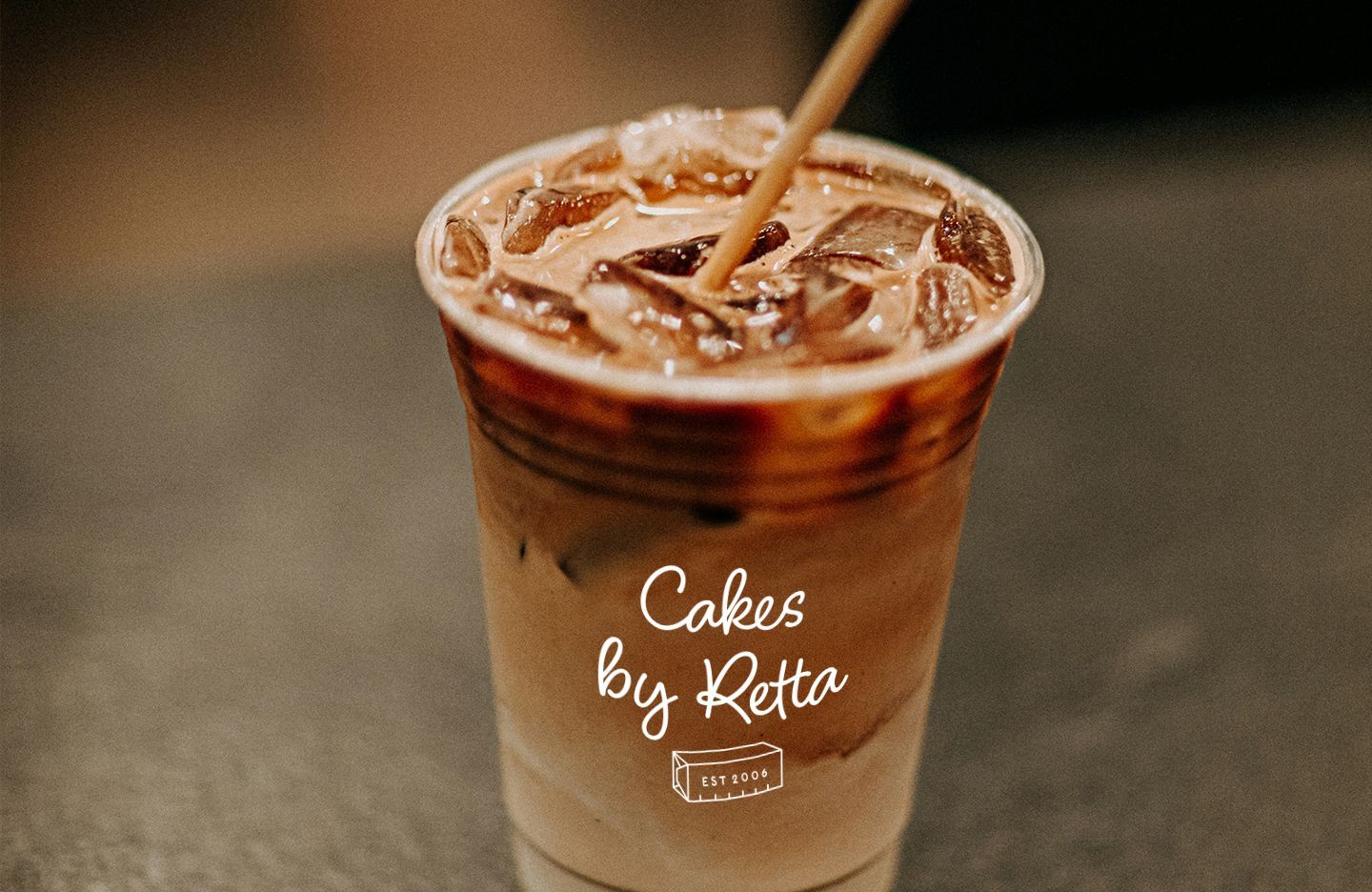 Iced coffee in a clear cup with straw; Cakes by Retta logo on the cup.