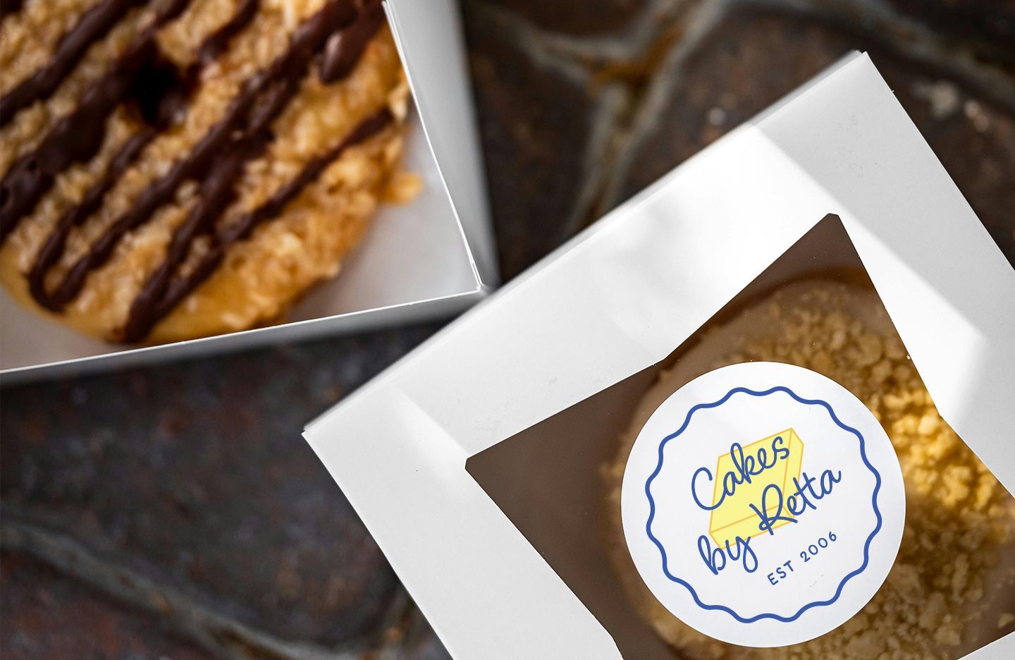 Two donuts in white boxes with Cakes by Retta logo.